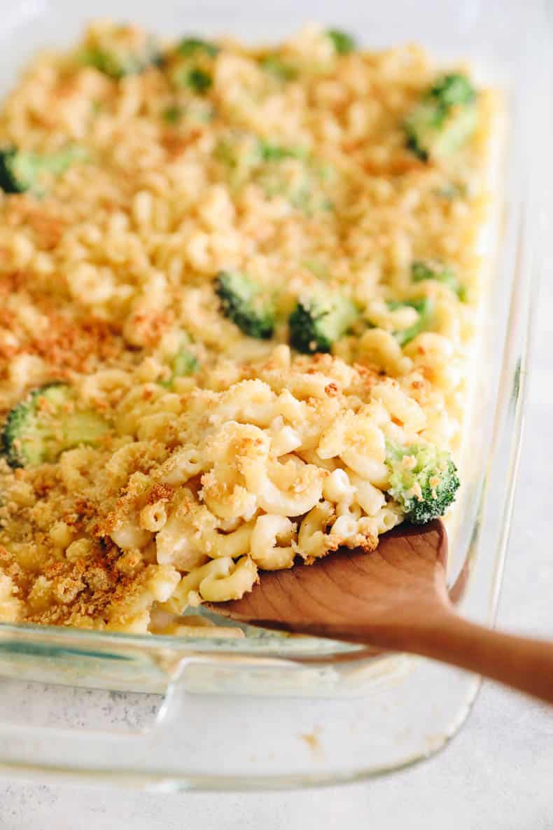 scooping out healthy mac and cheese from a baking dish.