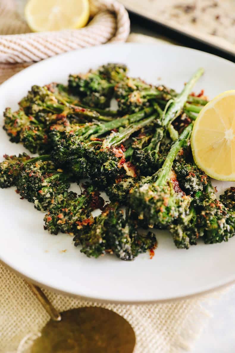 Roasted broccolini on a white plate sprinkled with parmesan and a sliced lemon.