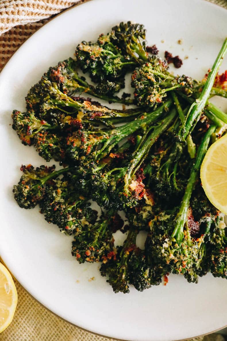 Overhead image of roasted broccolini on a white plate with charred parmesan and lemon.