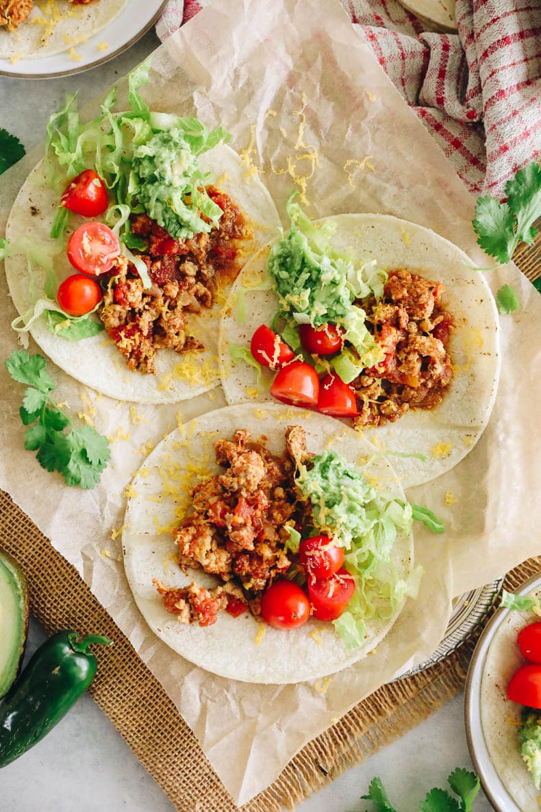 overhead image of turkey tacos on a parchment-lined plate with tomatoes, guac and shredded lettuce.