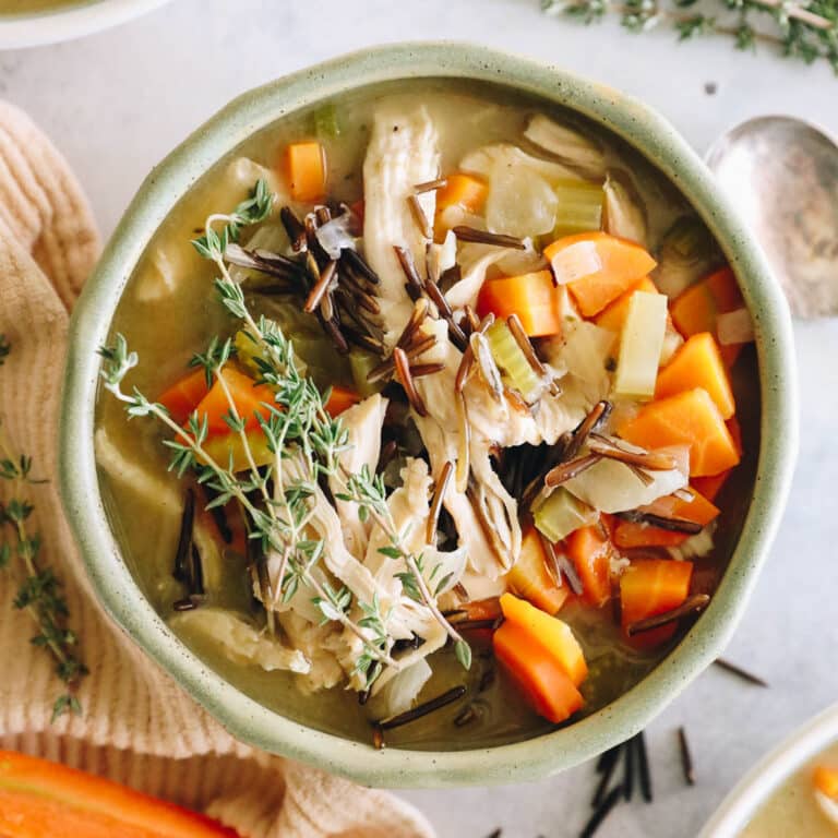 large overhead image of chicken and wild rice soup in a green bowl with cooked carrots.