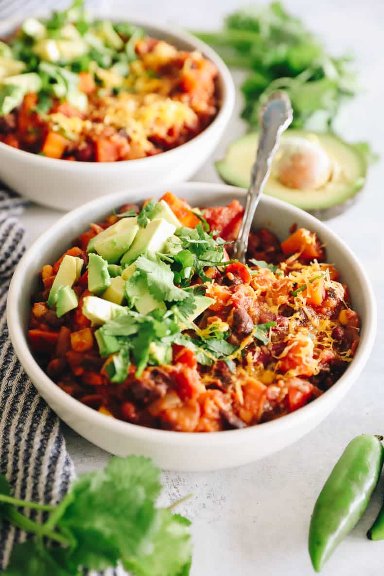 healthy chili recipe in white bowls topped with avocado, cilantro and shredded cheese.