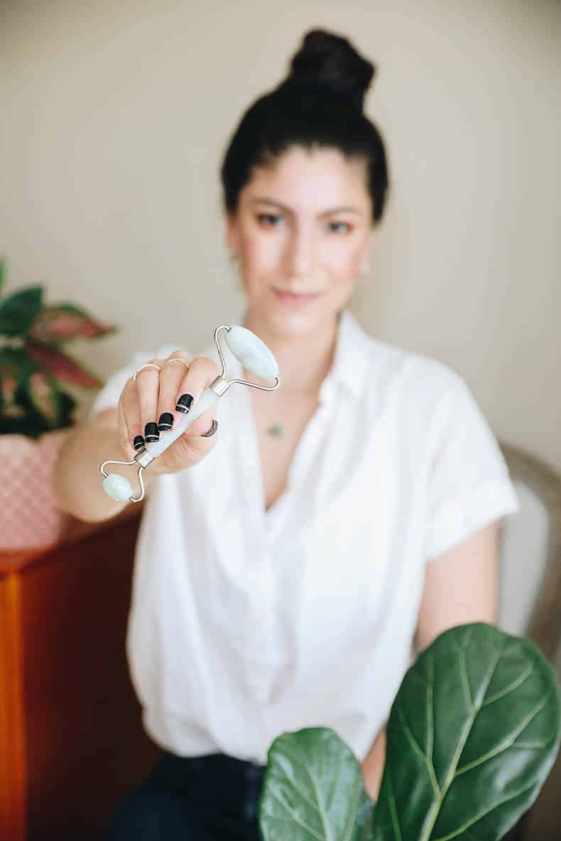 woman holding a green jade roller in her hands.