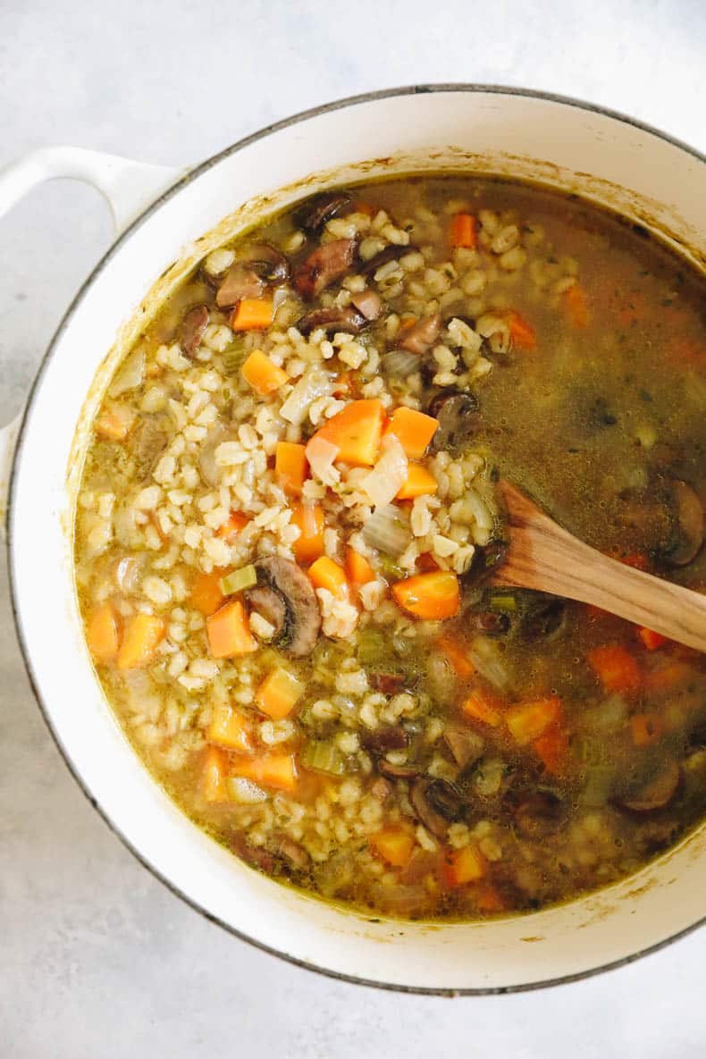 mushroom barley soup in a large soup pot with a wooden spoon