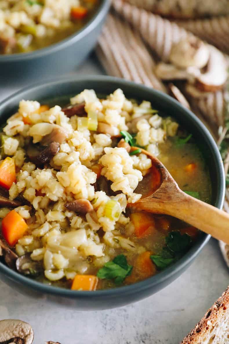 mushroom barley soup in a blue bowl with a wooden spoon