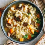 mushroom barley soup with carrots, celery and parsley in a blue bowl.