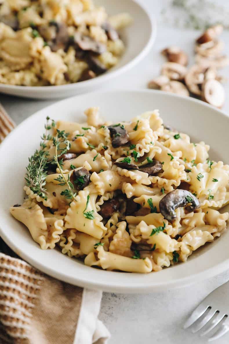 vegan stroganoff in a white shallow bowl topped with parsley and thyme.