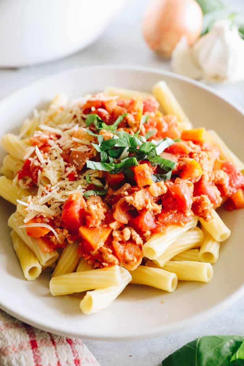 turkey bolognese on a bed of rigatoni noodles in a white bowl.