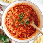 overhead image of turkey bolognese in a white dutch oven sprinkled with basil and a wooden spoon.