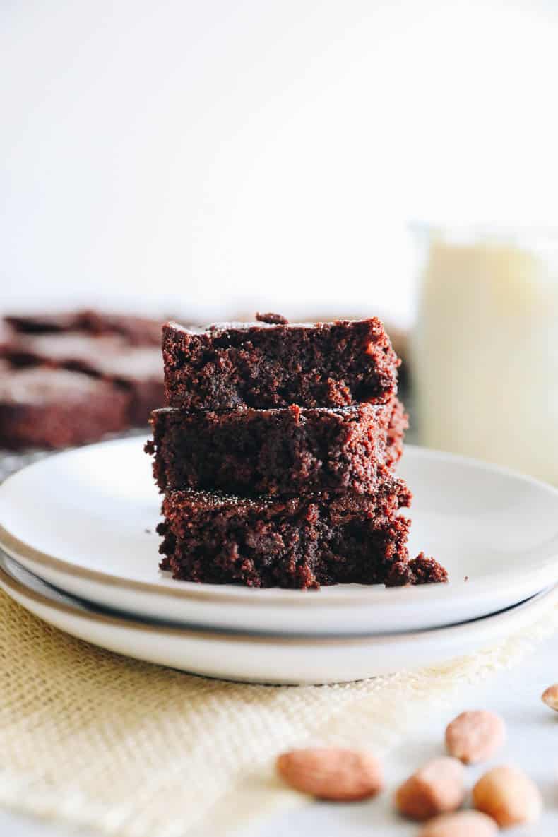 3 almond flour brownies stacked on a white plate.