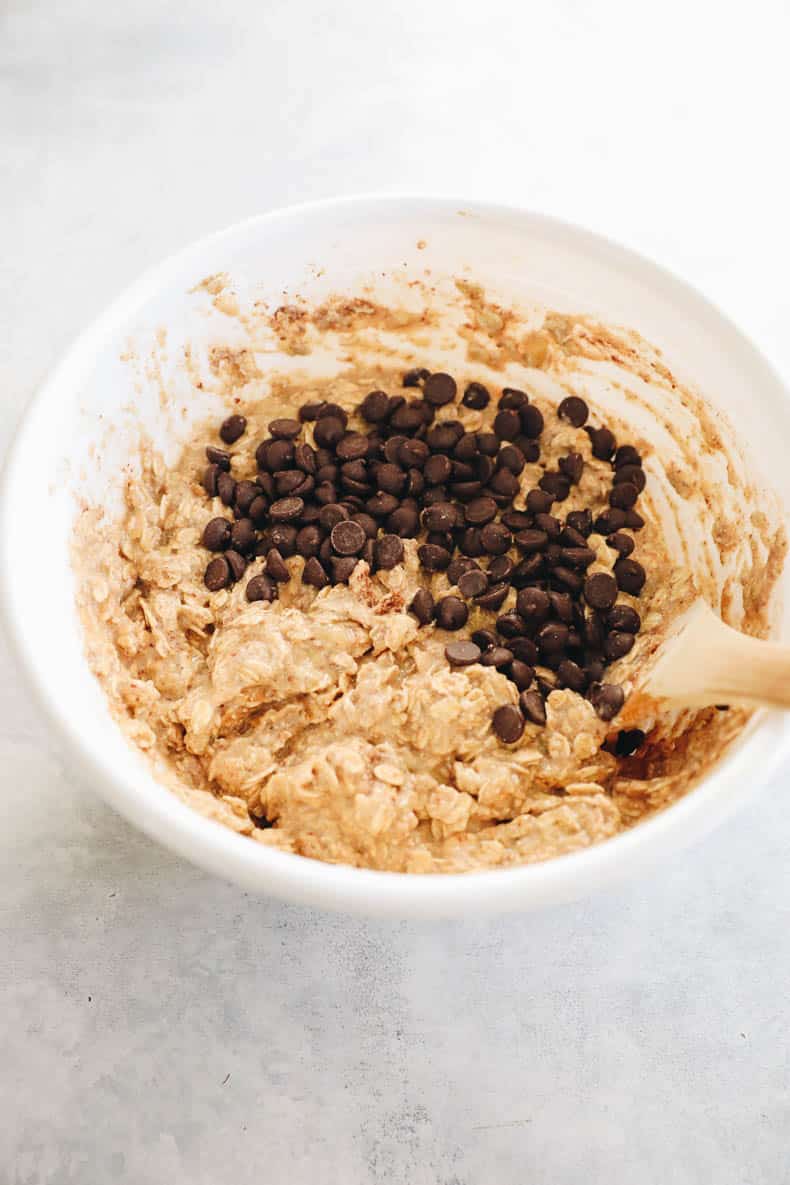 chocolate chips being mixed into oatmeal bar batter in a white bowl.