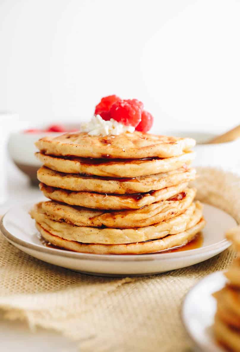 stack of cottage cheese pancakes on a white plate with fresh raspberries and maple syrup.