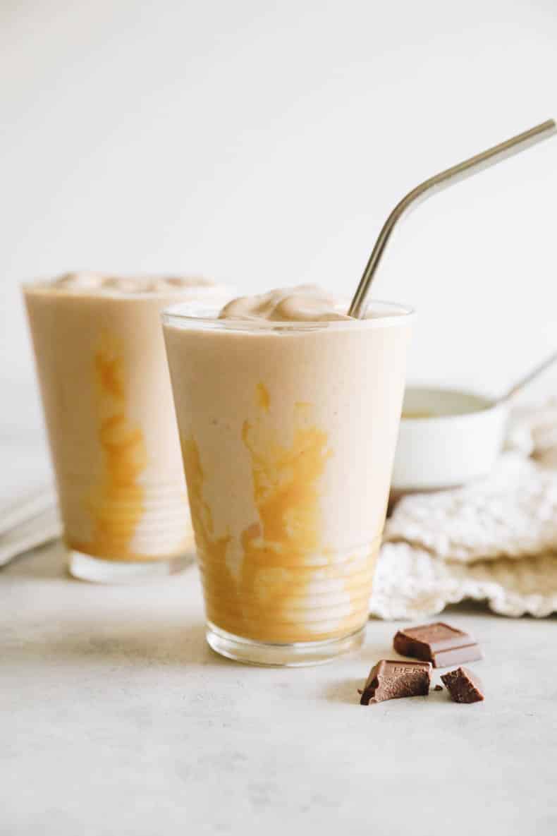 thick chocolate peanut butter smoothie in a glass with drizzled peanut butter and a metal straw.