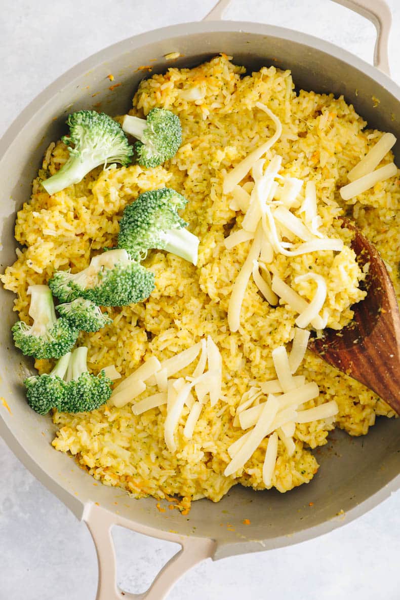 cheesy broccoli and rice in a large pan with a wooden spoon.