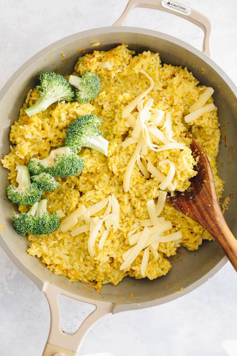 cheesy rice with broccoli and shredded cheddar in a large pan.