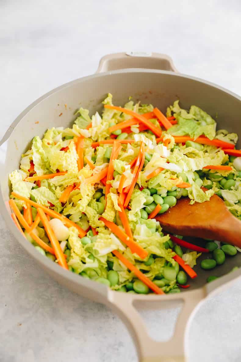 sliced carrots, cabbage, green onions and edamame in a skillet.