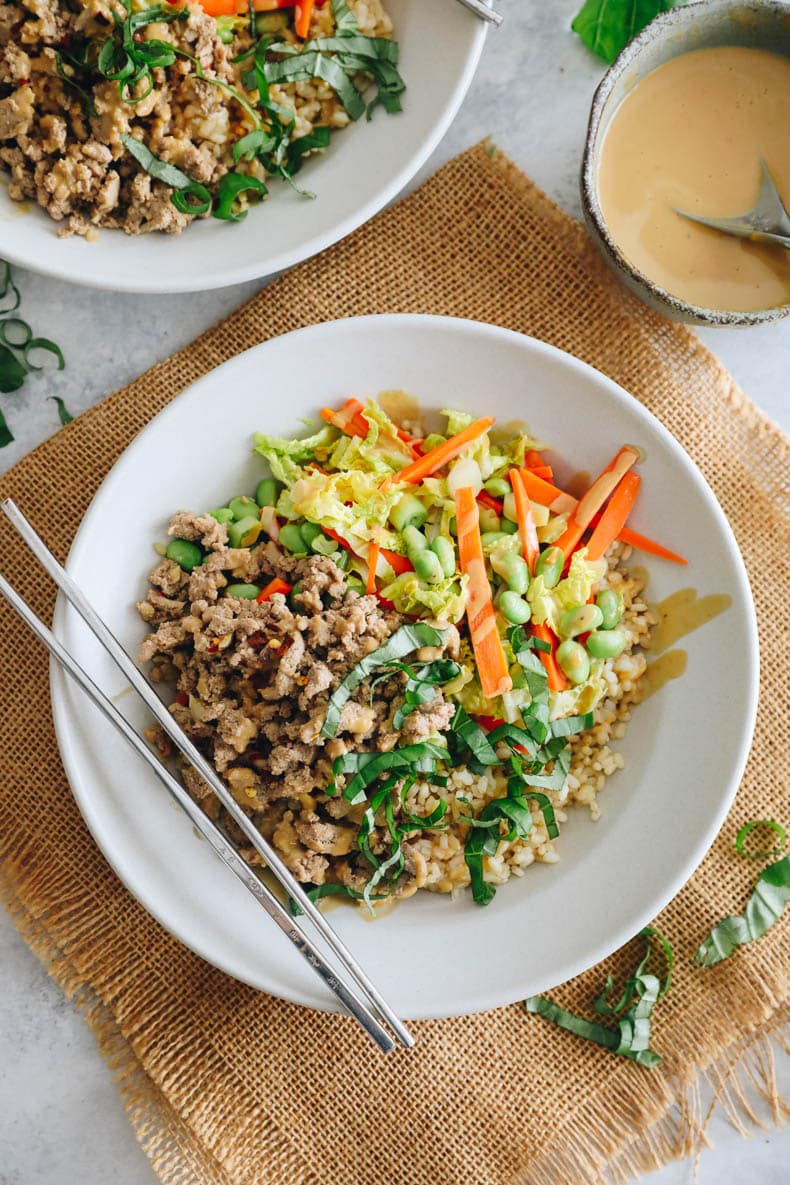 Thai basil turkey bowls in shallow white bowls with chopsticks and chopped thai basil.