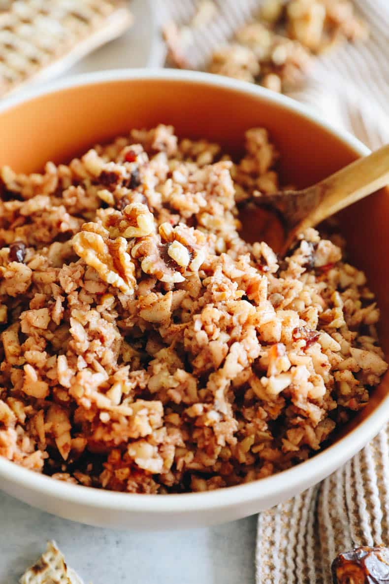 upclose image of charoset in an orange bowl with a wooden spoon.