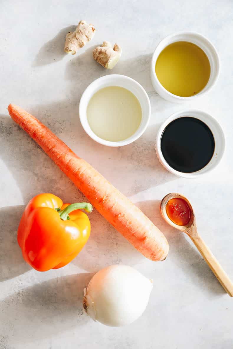 ingredients on a table - carrot, pepper, onion, honey, ginger, avocado oil, rice wine vinegar and tamari.