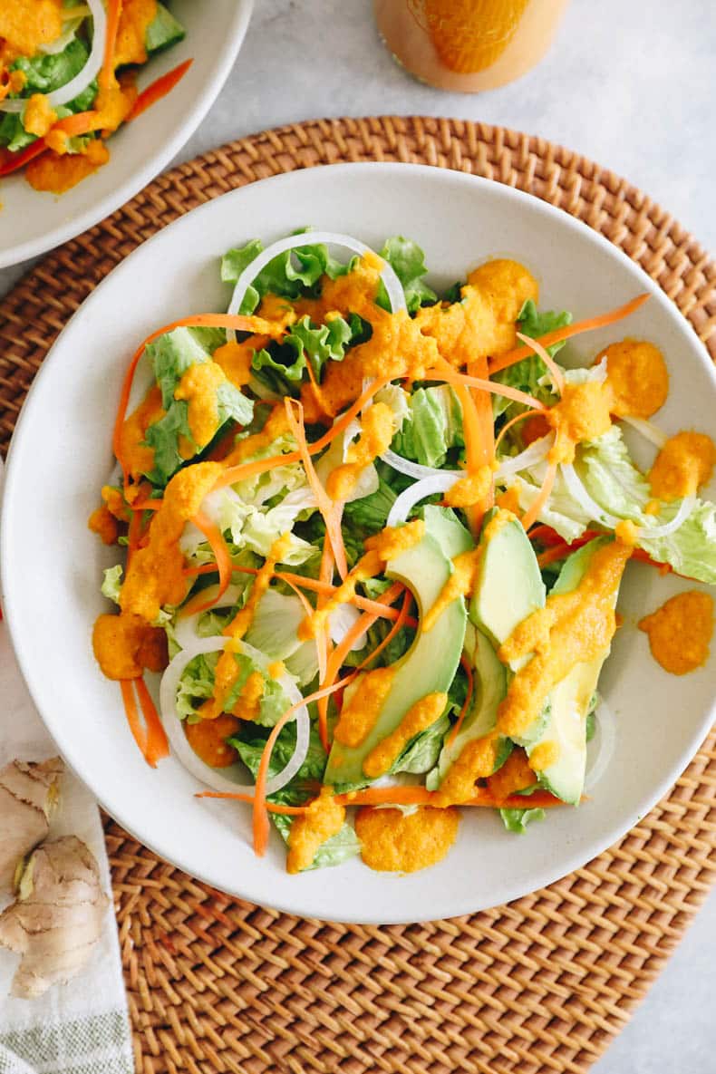 lettuce with onion, carrots, avocado in a white plate topped with a ginger dressing.