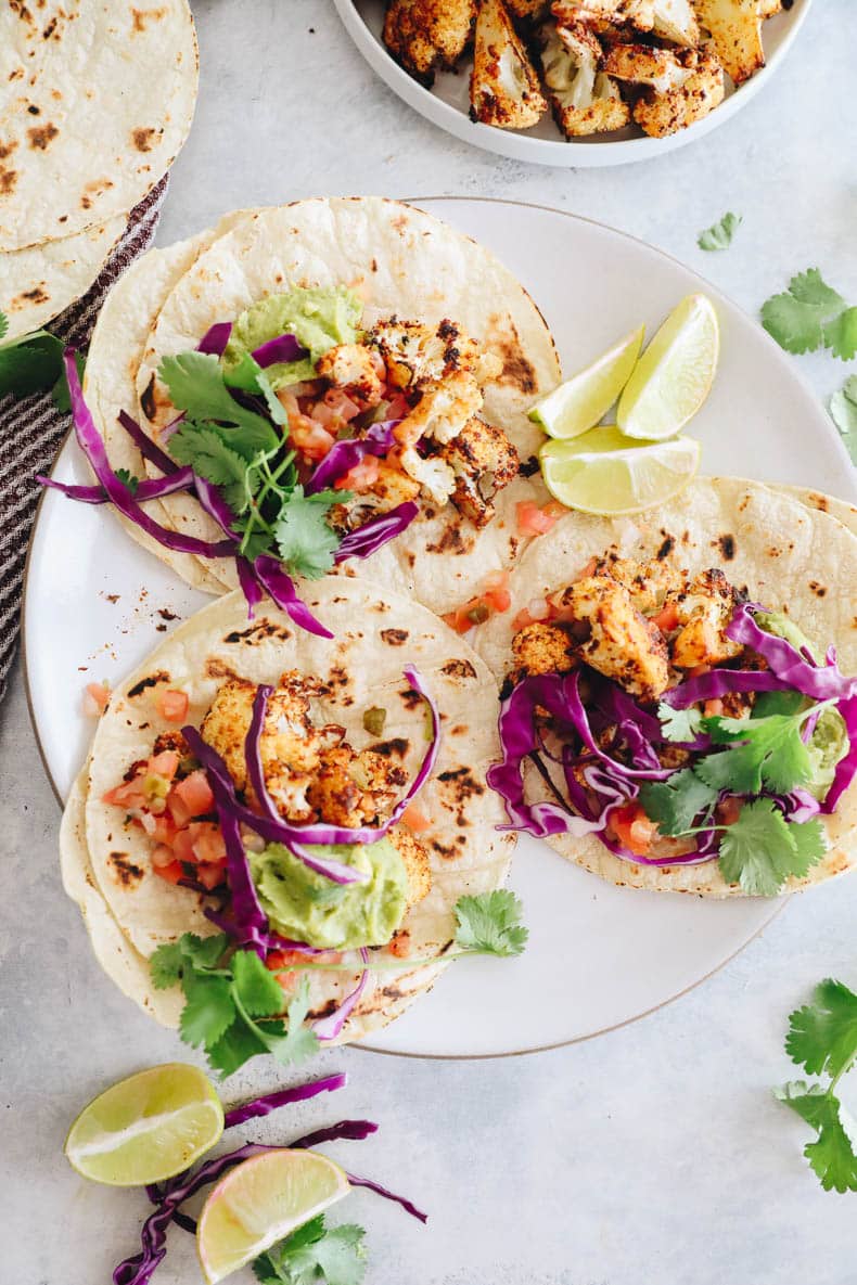 overhead image of cauliflower tacos with guac, pico de gallo, cilantro and purple cabbage.