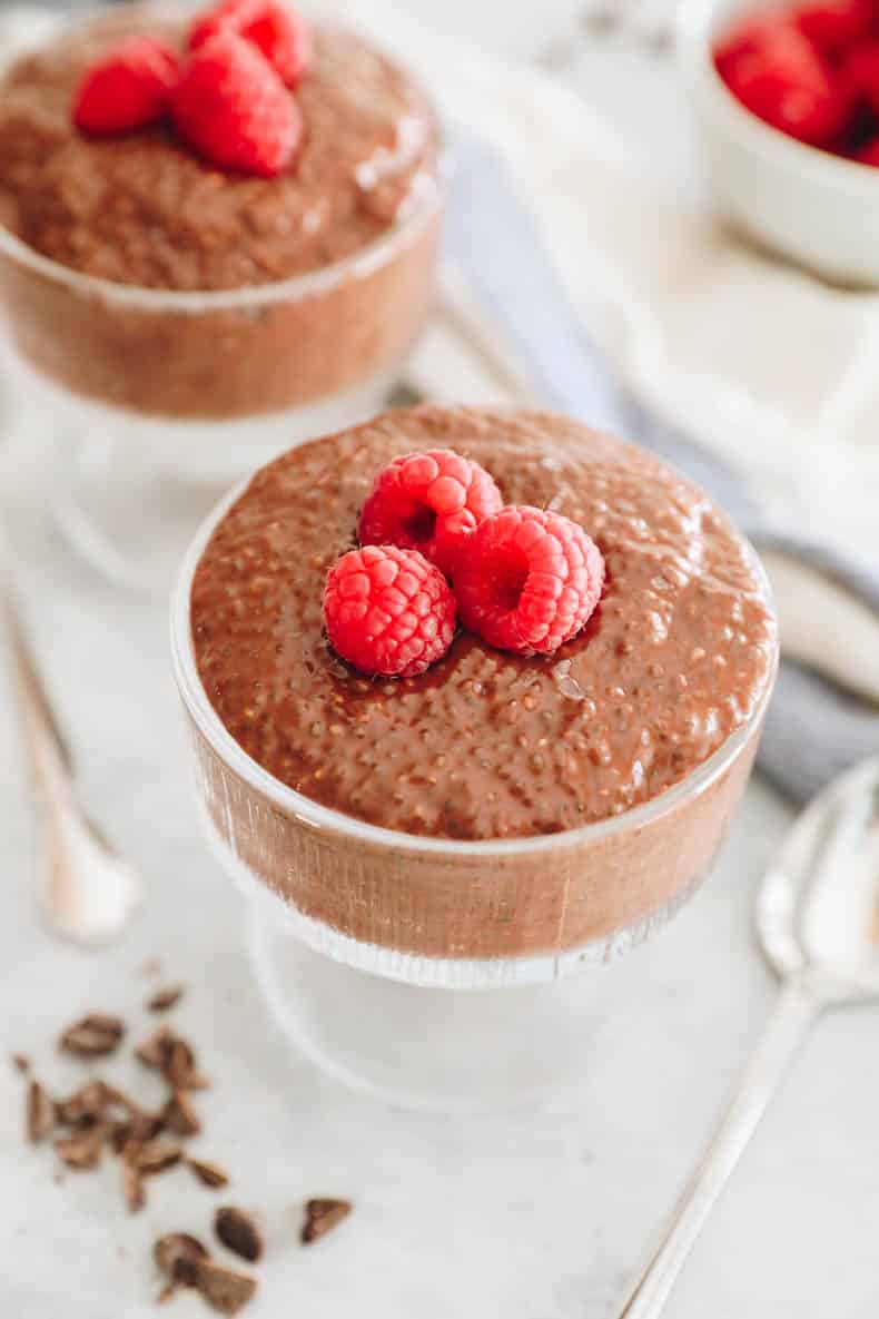 chocolate chia seed pudding in a glass cup topped with fresh raspberries.