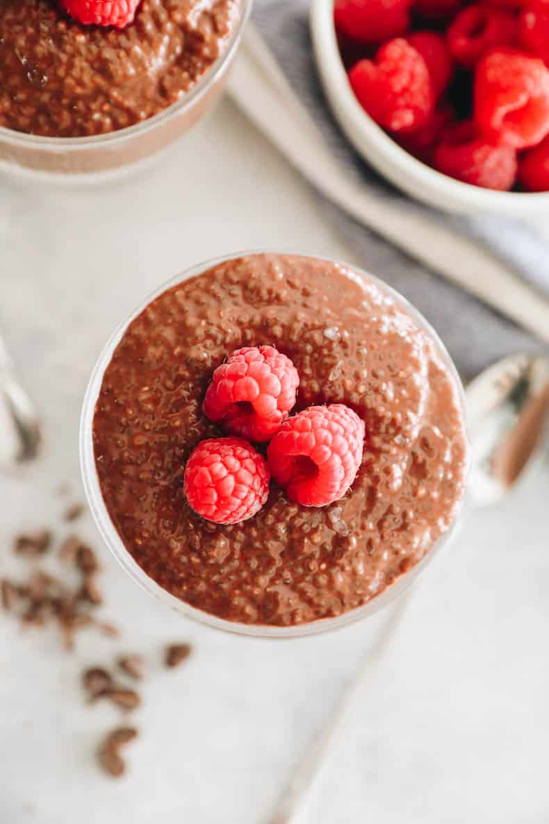 overhead of chocolate chia pudding in a glass cup with raspberries.