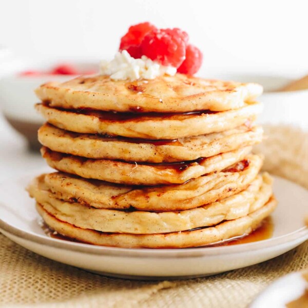 stack of cottage cheese pancakes on a white plate with raspberries and fresh cottage cheese.