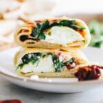 up close image of spinach feta wrap stacked on top of each other on a white plate.