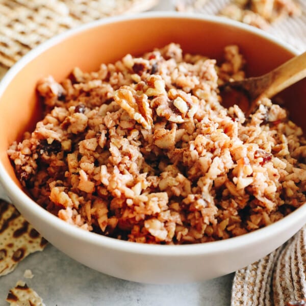 chopped up apple walnut charoset in a brown bowl with a wooden spoon and matzah.