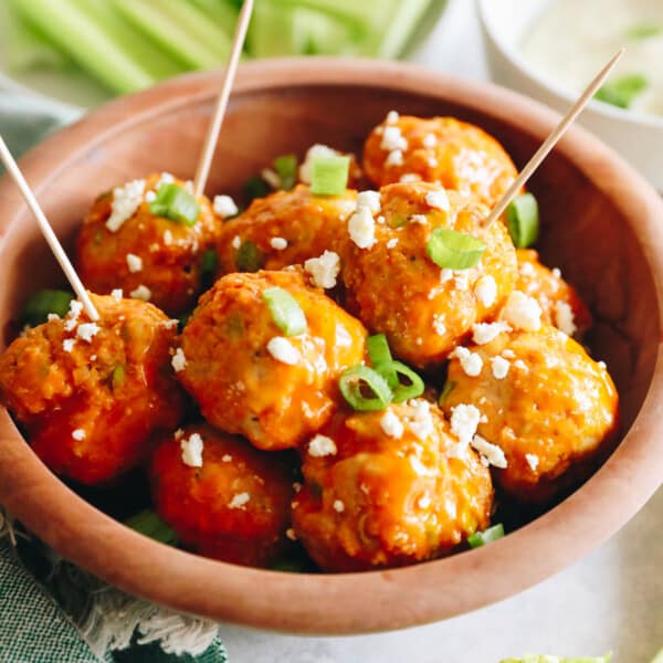 buffalo chicken meatballs in a brown bowl with toothpicks, green onions and feta cheese.